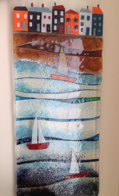 Boats bobbing on the sea with colourful orange and black house in the background on the shore.  All infused in glass.